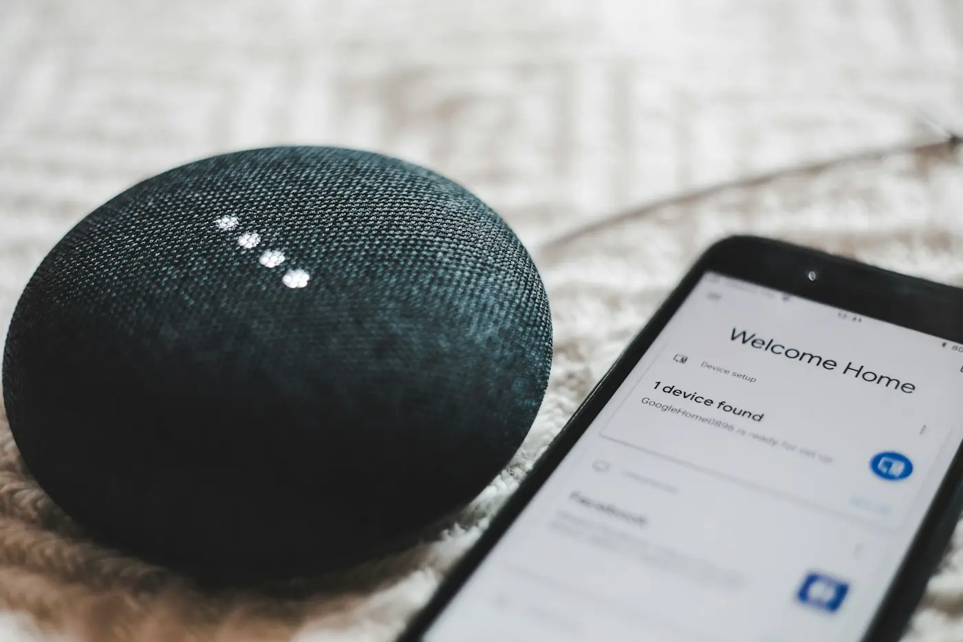 A Google Home Mini smart speaker beside a smartphone showing the Google Home app